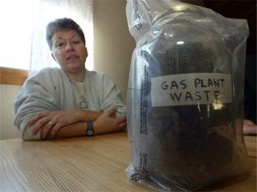 罗德岛州蒂弗顿的居民在一个标有“quot”的容器旁边摆姿势天然气厂废物“;2005年。该州认为，该地区的污染是由福尔河天然气公司倾倒煤气化废物数十年造成的。