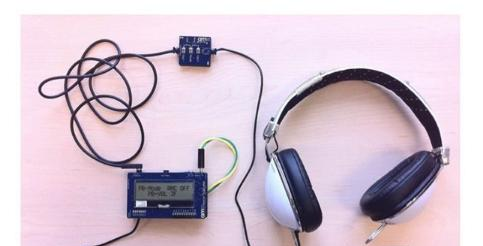 奥地利微电子的演示系统展示了主电路板(底部)，带有音量放大、模式和音量减小键的外围电路板(上)，以及头戴式耳机。.png